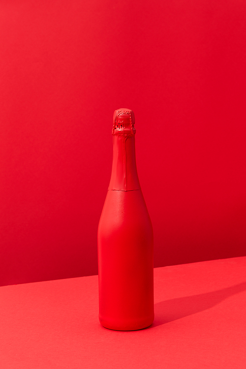 Holiday mock up bottle of champagne red painted spray on a duotone red background with soft shadows, copy space. Minimal concept.