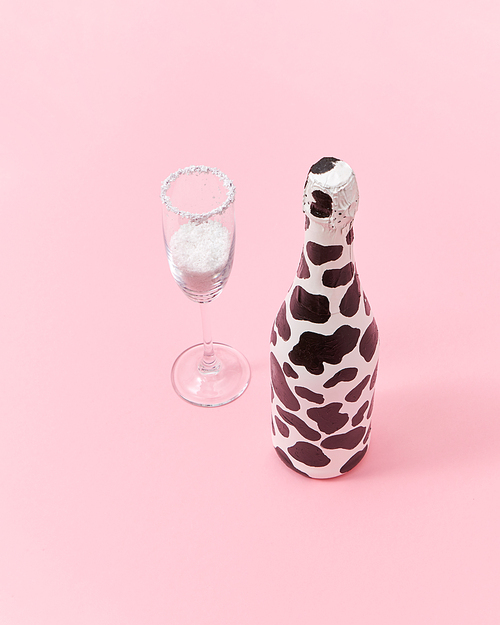 Decorative white painted champagne bottle with black spots and glass of white powder as a snow on a light millennial pink background, copy space. Congratulation card.