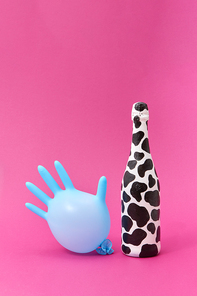 Wine bottle painted white and black spots with blue balloon rubber glove on a hot pink background, copy space.