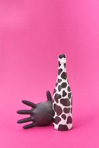 Champagne bottle painted white and black spots with black balloon rubber glove on a hot pink background, copy space.