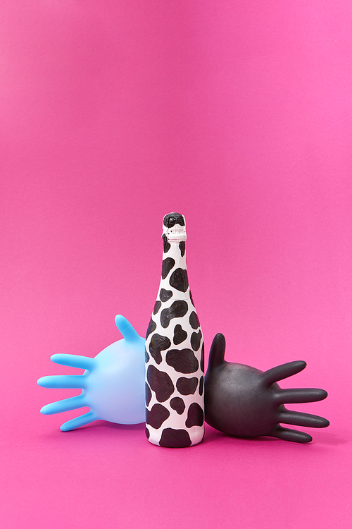 Creative composition with painted wine bottle of black spots and two rubber surgical balloon gloves on a hot pink background, copy space.