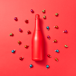 Creative pattern from red painted mock up bottle on a red background covered colored glass New Year balls with copy space. Greeting holiday card.