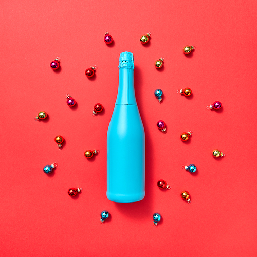 Decoration composition from blue painted bottle on a red background covered colorful glass New Year balls with copy space. Greeting holiday card
