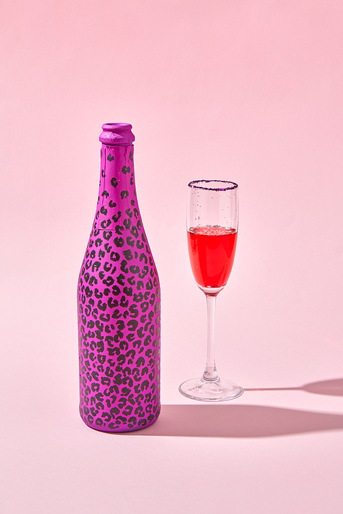 Glass of red wine with bottle painted hot pink with black spots and hard shadows on a pastel pink background, copy space.