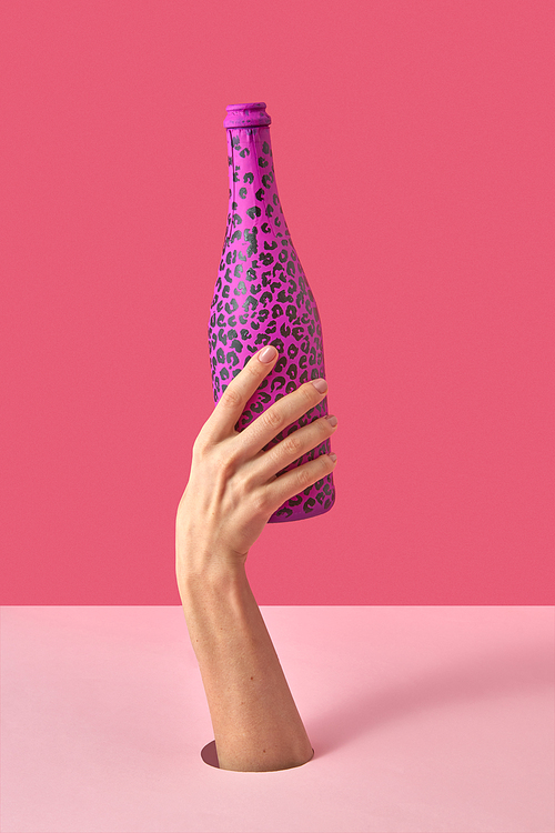 Painted hot pink wine bottle with black spots in a woman's hand on a duotone pink background, copy space. Holiday concept.
