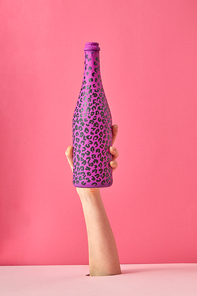Woman's hand holds painted bottle with black spots on a pink background, copy space.