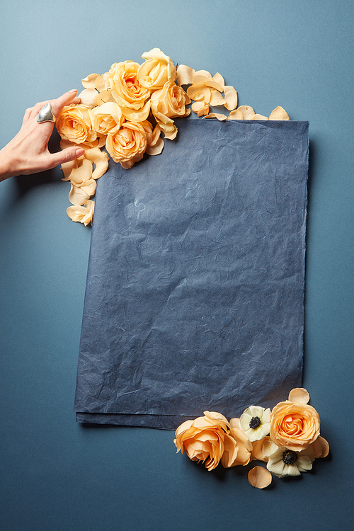 Female hand decorating blank sheet of paper with flowers. Empty frame for text