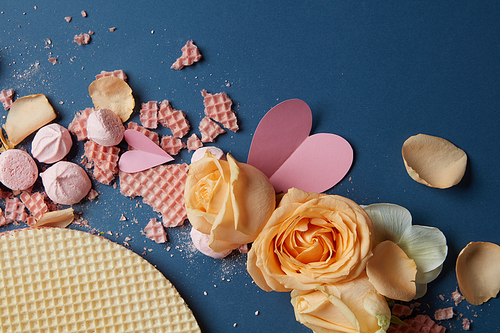 Waffles and roses with many hearts used for decoration of background. Closeup of roses and waffles represented on navy blue background.