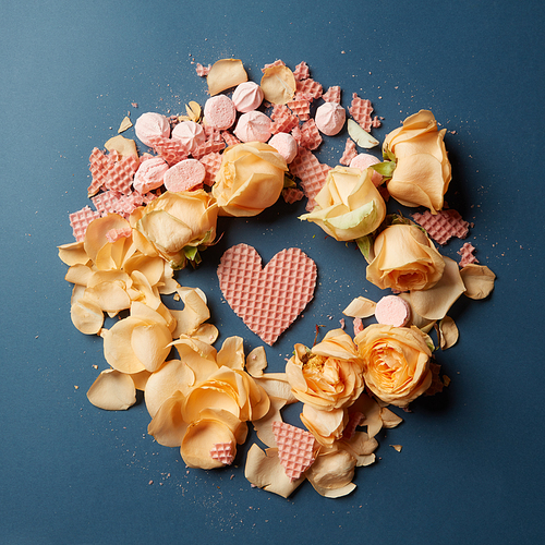 round frame of a beautiful beige roses and hearts of wafers on a dark background, flat lay