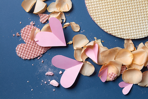 paper and wafer heart with rose petals on a blue background