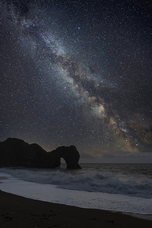 Digital composite of Milky Way over epic seascape landscape image of cliffs and archway