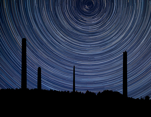 Digital composite image of star trails around Polaris with industrial chimney stacks landscape