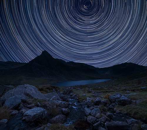 Digital composite image of star trails around Polaris with Stunning vibrant Beautiful landscape image of stream near Llyn Ogwen in Snowdonia with Tryfan