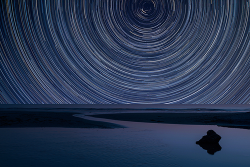 Digital composite image of star trails around Polaris with landscape of low tide beach