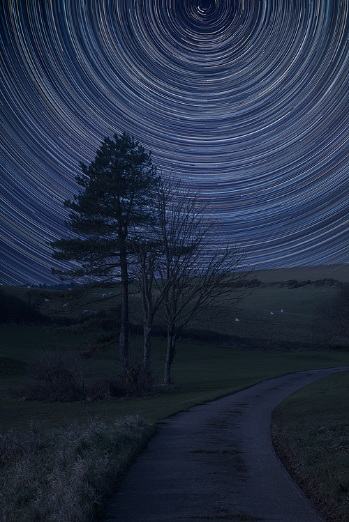 Digital composite image of star trails around Polaris with Beautiful landscape image of farm and trees in Winter