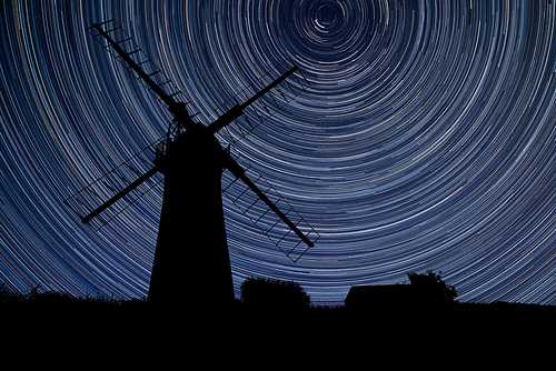 Digital composite image of star trails around Polaris with Windmill in stunning landscape