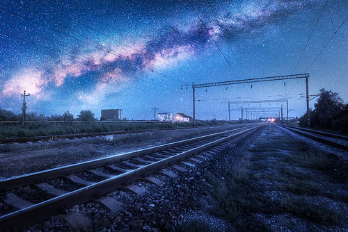 Milky Way over the railway station at starry night. Beautiful industrial landscape with blue sky and stars, galaxy, railroad and buildings at dusk. Railway platform and space in summer. Technology