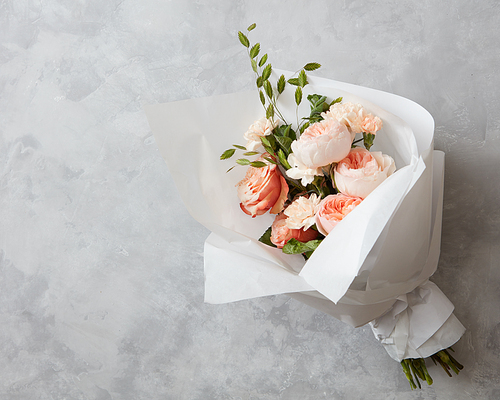 Beautiful pink roses of bouquet with white paper on a gray stone background
