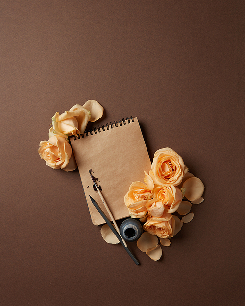 Diary or notebook with pen and ink for your notes. Notebook with brown pages with orange roses represented on brown background.