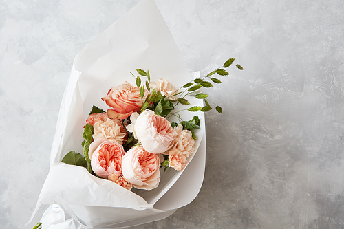 Beautiful pink roses of bouquet with white paper on a gray stone background, flat lay