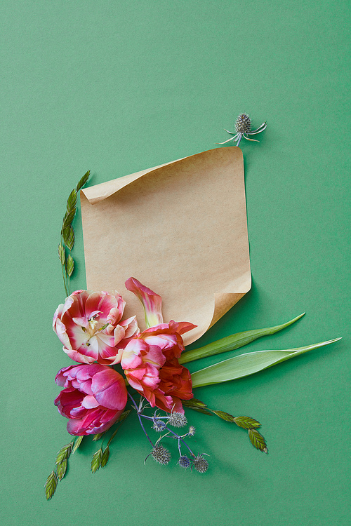 bouquet of purple flowers on a green background with a piece of kraft paper for text, flat lay