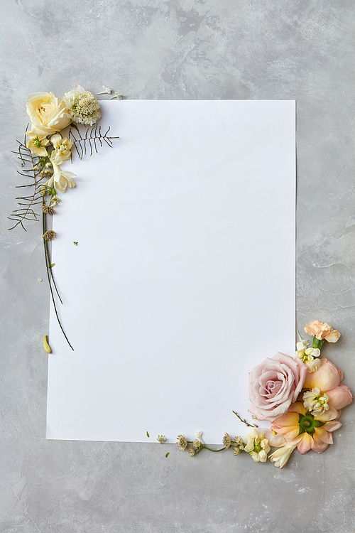 beautiful frame with flowers and a white paper with room for text on gray concrete background, flat lay