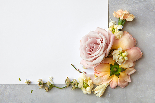 Corner frame of flowers and a white paper on a gray background, flat lay