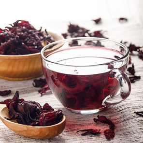 Closeup view at wooden bowl tea cup and spoon of dry hibiscus petals on linen cloth background