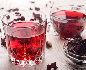 Closeup view at two tea cups with ice and dry hibiscus petals on white wooden table background