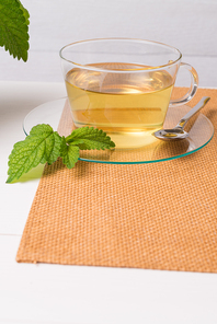 Herbal tea with melissa in a glass cup a green napkin on a light green wooden table top.