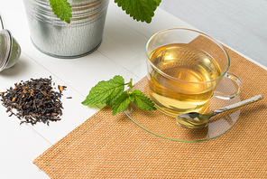 Herbal tea with melissa in a glass cup a green napkin on a light green wooden table top.