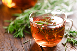 Rosemary tea in glass tea cup on rustic wooden table closeup. Herbal vitamin tea.