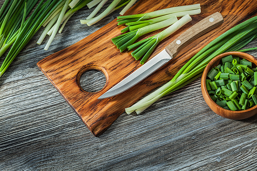 chopped green spring scallions kitchen knife wooden cutting board vintage wood background