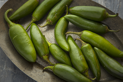 A close up studio photo of green chili peppers on a platter.