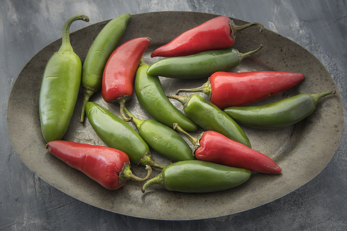 A close up studio photo of red and green chili peppers on a platter.
