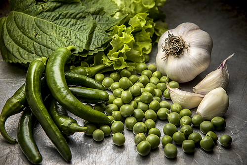 A close up studio image of an assortment of vegetables such as garlic, lettuce, peas, and peppers.