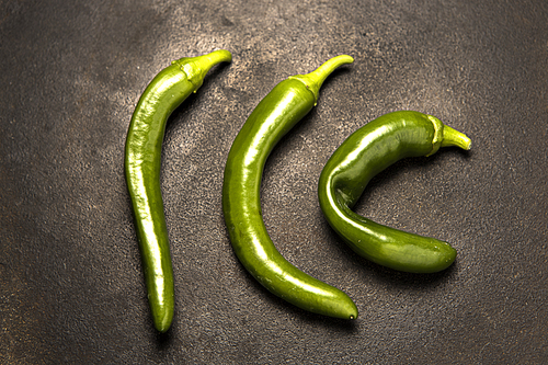 A studio photo of three raw green chili peppers.