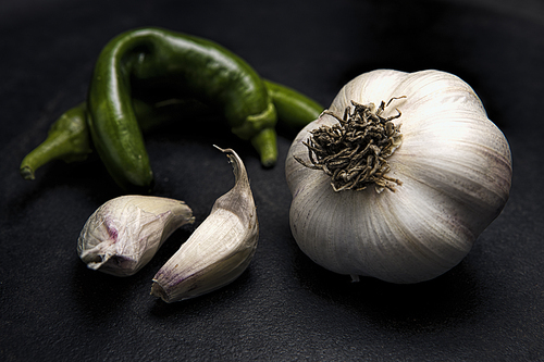 A fine art studio photo of a raw garlic bulb, a couple of cloves and green chili peppers.