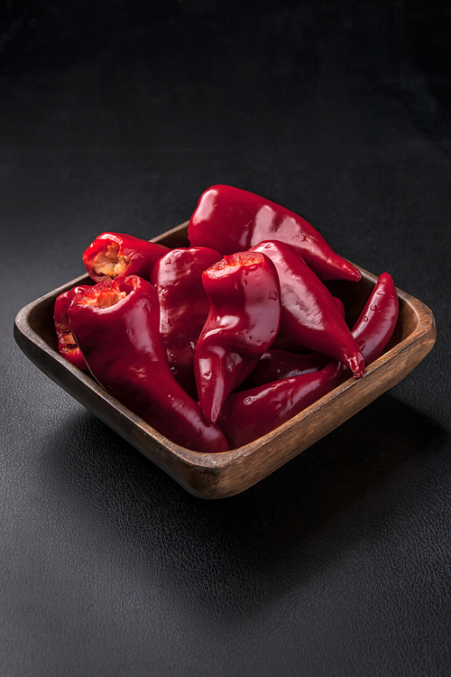 A close up of a wooden bowl full of bright red chili peppers.