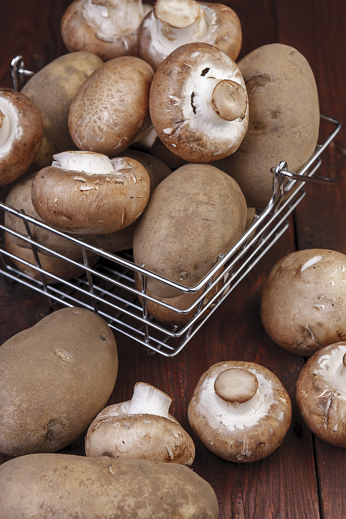 A metal wire basket filled with potatoes and mushrooms on a wooden table.