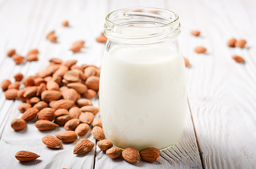 Milk or yogurt in mason jar on white wooden table with almonds aside