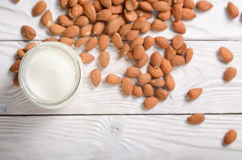 Milk or yogurt in mason jar on white wooden table with almonds aside flat lay view