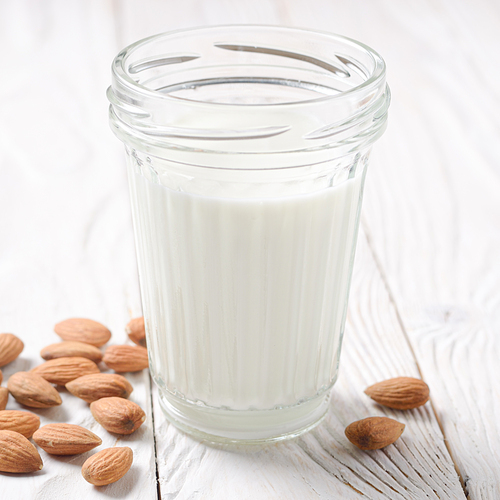 Milk or yogurt in mason jar on white wooden table with almonds aside