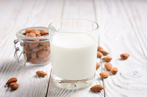 milk or yogurt in  glass on white wooden table with almonds in airtight conainer aside