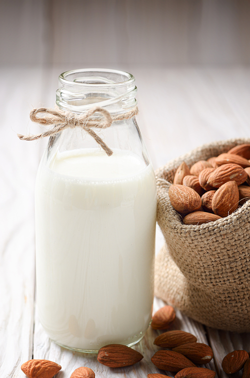 Milk or yogurt in glass bottle on white wooden table with almonds in hemp sack aside