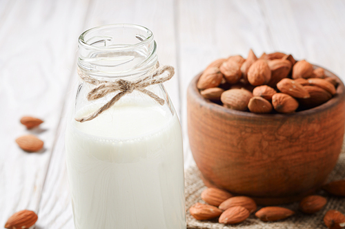 Milk or yogurt in glass bottle on white wooden table with bowl of almonds on hemp napkin aside
