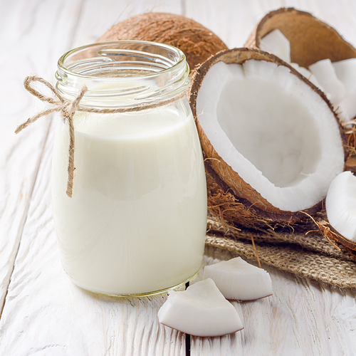 Mason jar of milk or yogurt on hemp napkin on white wooden table with coconut aside