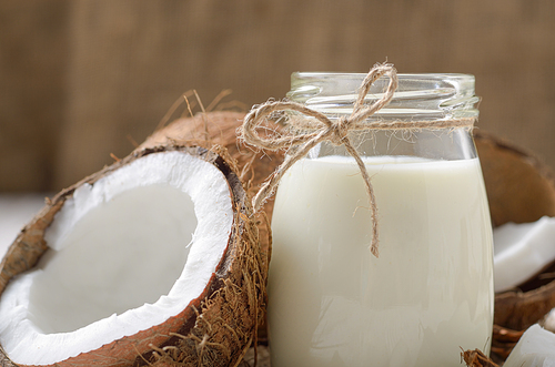 Milk or yogurt in mason jar on white wooden table with coconut aside