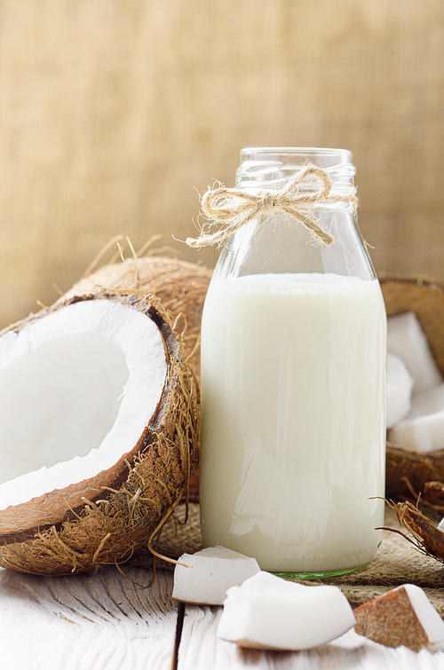 Glass bottle of milk or yogurt on hemp napkin on white wooden table with coconut aside