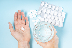 someone taking prescripted meds, hands with white pills and glass of clear water over blue background
